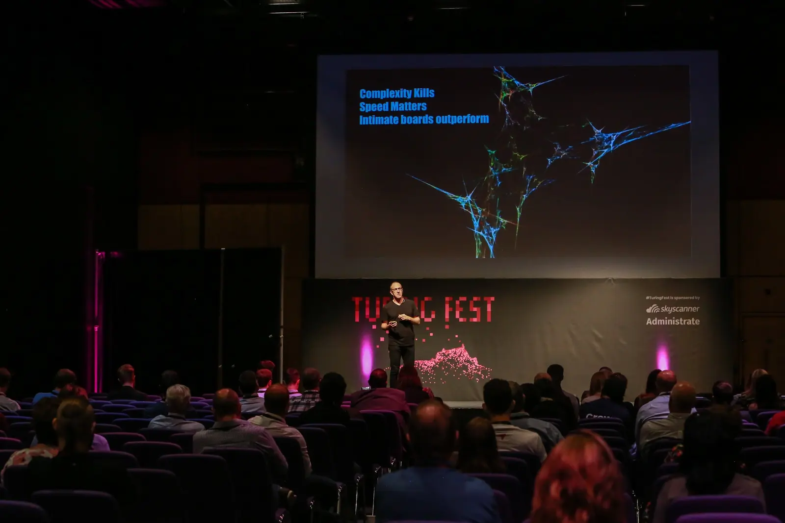 Fred Destin on stage at Turing Fest beside a slide reading 'Complexity Kills, Speed Matters, Intimate boards outperform'
