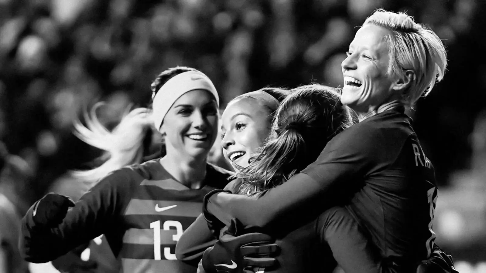 US women's soccer team players smiling and embracing in celebration, in black and white