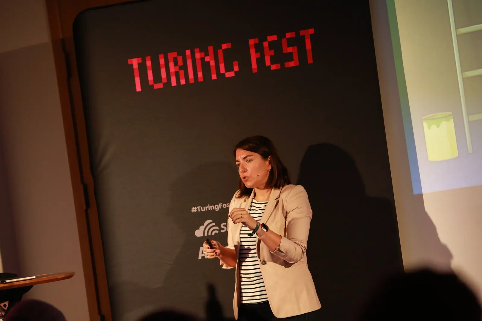 Maria Gutierrez speaking on stage at Turing Fest in front of a Turing Fest banner