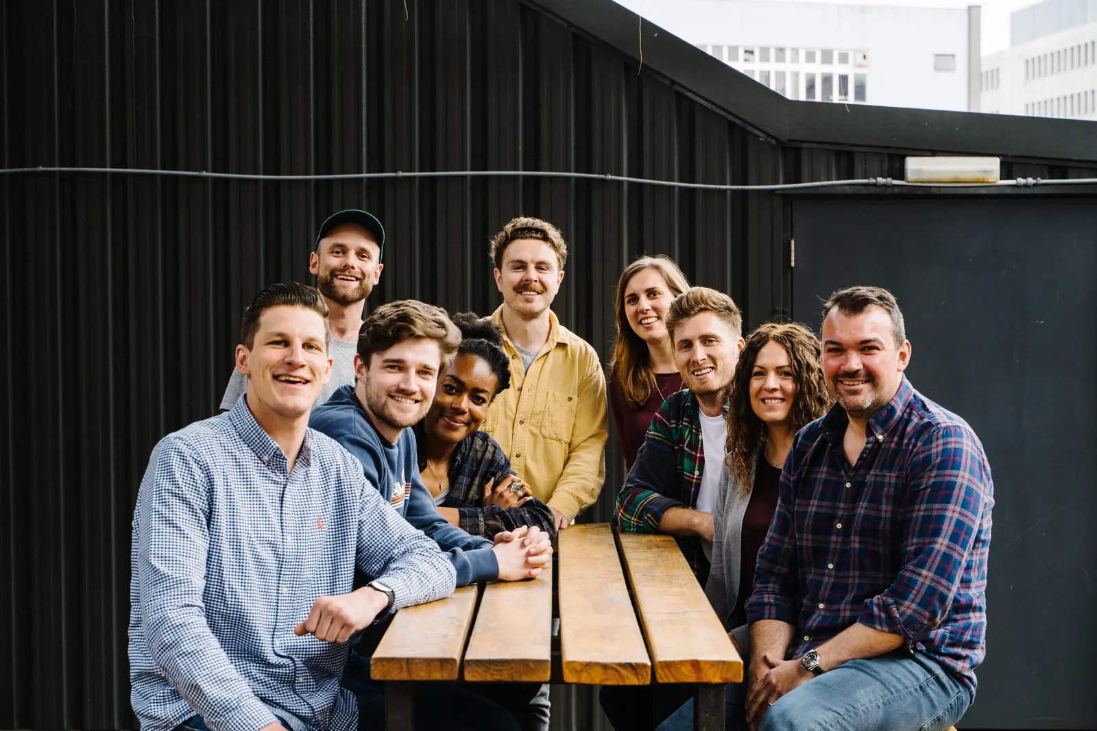 The Brewgooder team gathered around a wooden picnic table on a rooftop, smiling at the camera